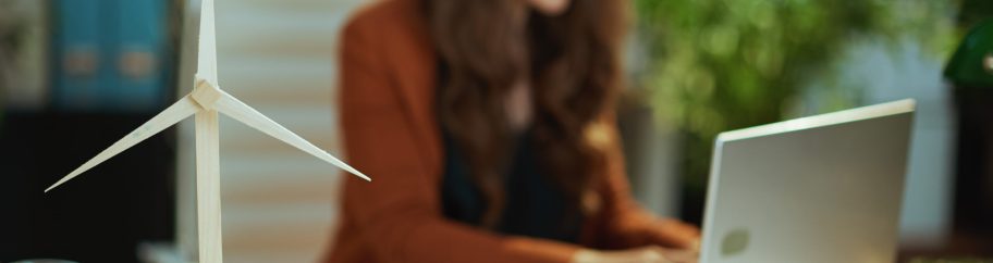 Closeup on wind turbine and woman with laptop working in background in the green office.